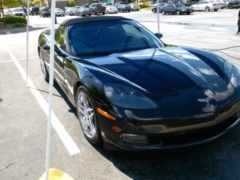 Black Corvette sports car parked in outdoor lot with white parking space lines