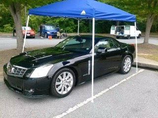 Black sedan parked under blue pop-up canopy tent in outdoor lot
