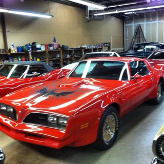 Red muscle car with white racing stripes displayed in automotive workshop garage