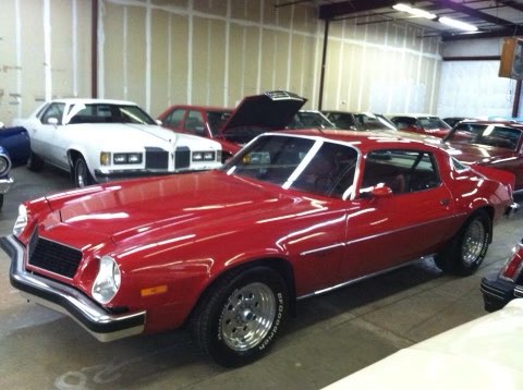 Red Chevrolet Camaro with white stripe in vintage car showroom with other classic cars