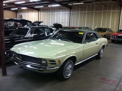 Light green 1960s Ford Mustang convertible displayed in classic car showroom with other vintage vehicles