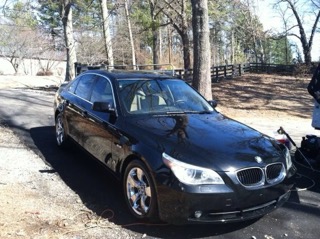 Black BMW sedan parked in driveway with bare trees in background