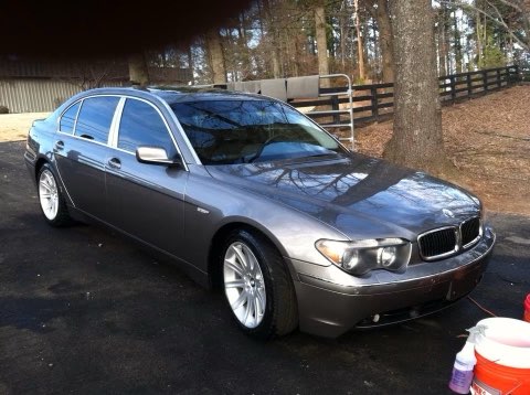 Silver BMW sedan parked in driveway with trees and wooden fence in background