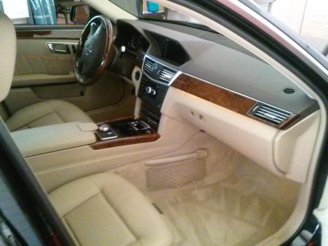 Luxury car interior with cream leather seats, wood trim dashboard, and steering wheel visible from driver side view