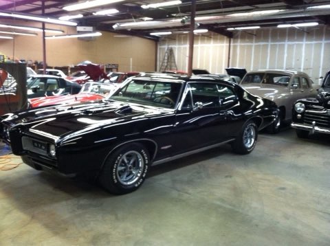 Black muscle car with hood open displayed in indoor showroom with other classic vehicles