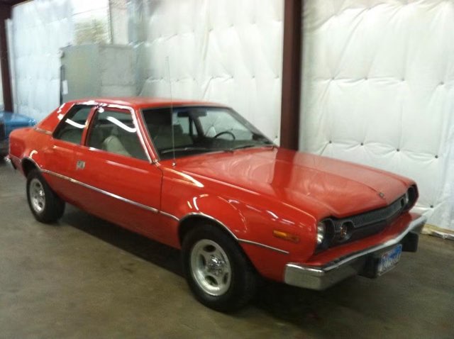 Red 1970s sedan parked indoors against white wall