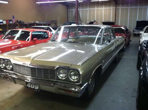 Classic 1960s gold sedan displayed in indoor car showroom with other vintage vehicles