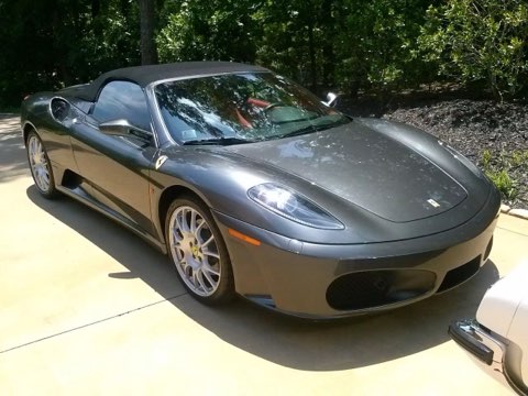 Gray Ferrari F430 Spider convertible parked on driveway with trees in background