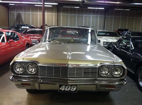 1964 Chevrolet Impala on display in vintage car showroom with red and black vehicles