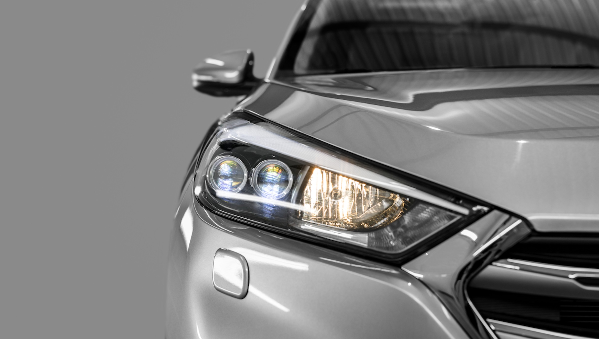 Silver SUV headlight detail with LED daytime running lights against gray background