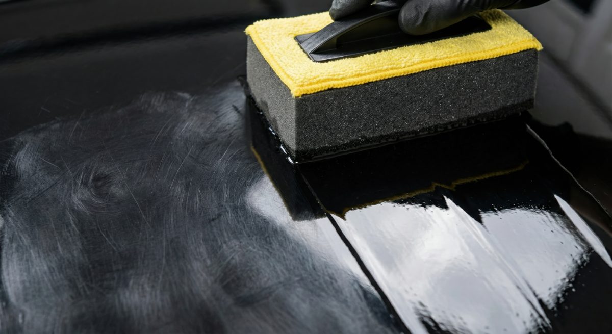 Person applying white primer or coating to dark surface with yellow and black foam applicator block