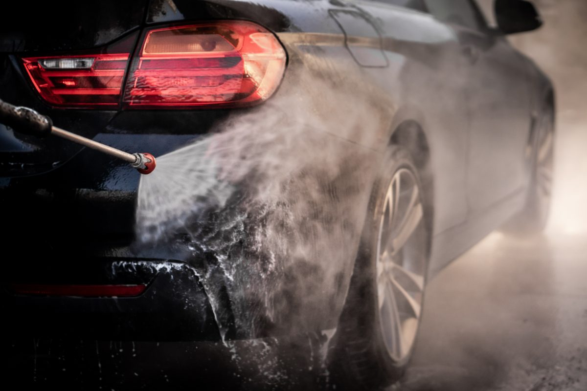 Black car being washed with high-pressure water spray from hose